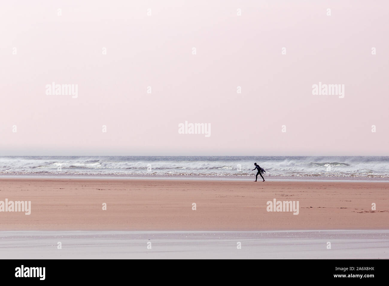 Surfeur solitaire, transportant une planche de surf, marchant le long de la plage à Mawgan Porth, Cornwall, Royaume-Uni Banque D'Images
