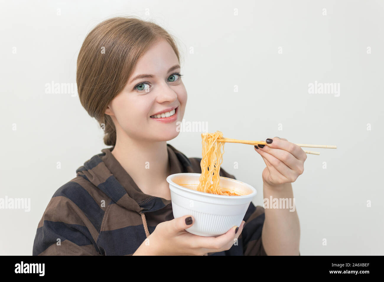 Young caucasian girl woman eating instant ramen noodles with chopsticks Banque D'Images