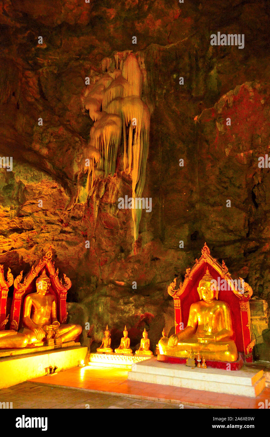 Plusieurs images de Bouddha assis à Khao Luang Cave Petchaburi Thaïlande, une grande stalactite au-dessus d'eux sur le mur. Il y a une lueur orange de la lumière Banque D'Images