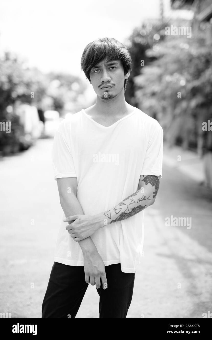 Jeune homme asiatique avec des tatouages à la main à l'extérieur en noir et blanc Banque D'Images