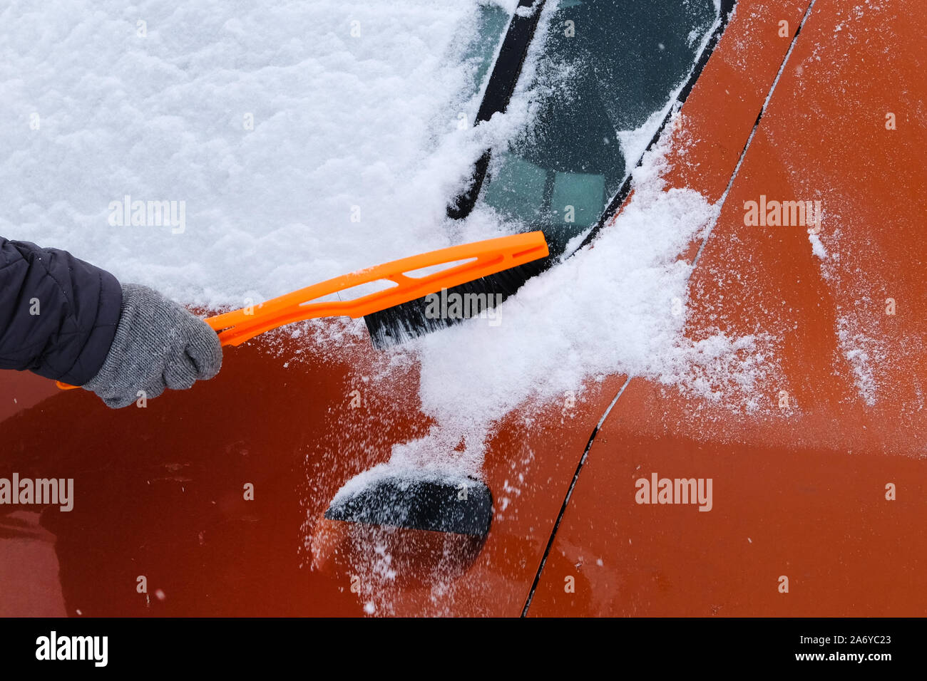 Voiture couverte de neige. Pinceau en main. mans L'homme en gris gants est orange brossage voiture de la neige. Banque D'Images