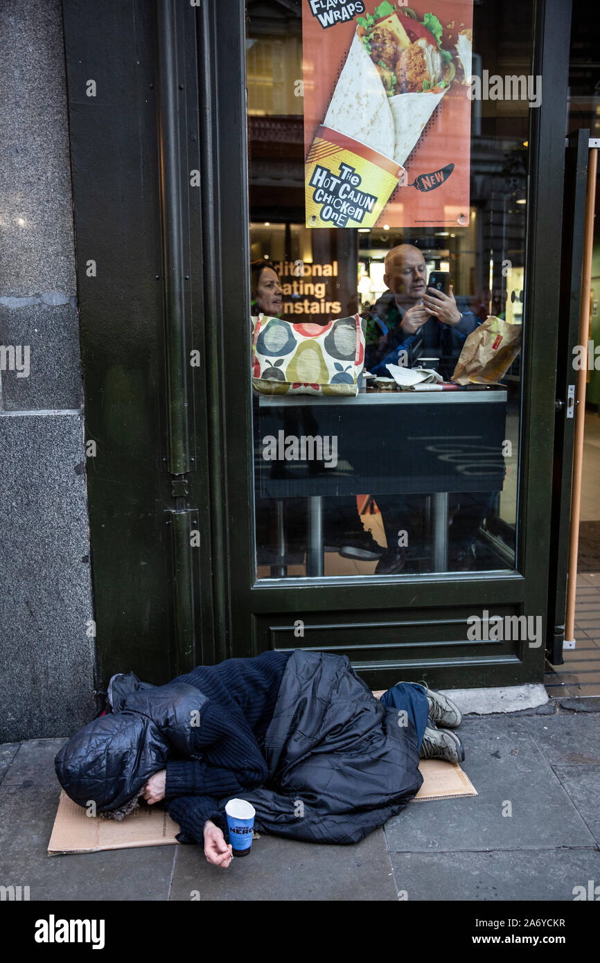 Le dormeur rugueux se trouve dans la rue, à l'extérieur d'une chaîne de restauration rapide, tandis que les gens s'assoient à l'intérieur de la nourriture chaude à la fenêtre, dans le centre de Londres, au Royaume-Uni Banque D'Images