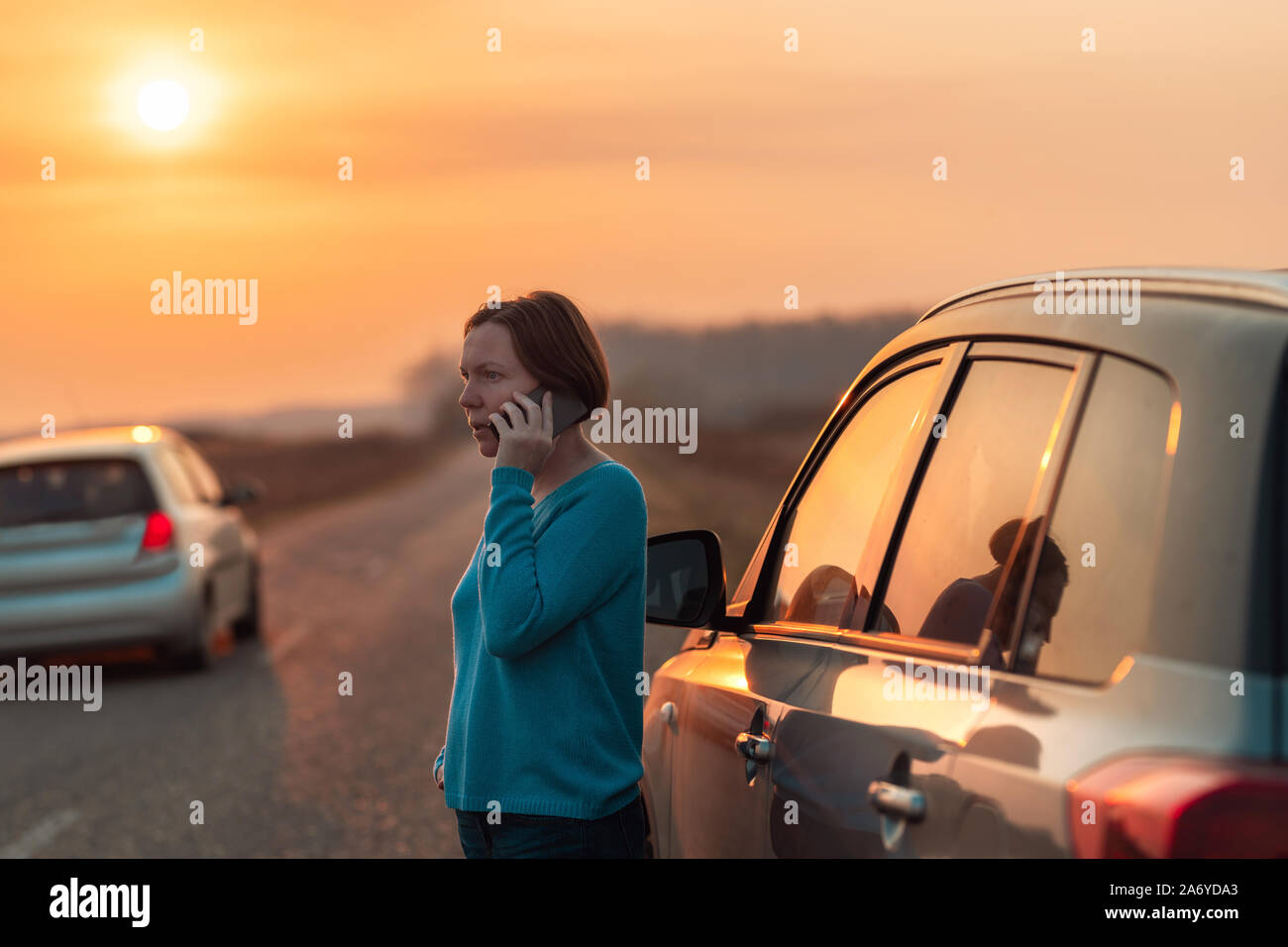 Femme appelant sur téléphone mobile pour l'assistance et l'aide sur la route après sa voiture est tombé en panne en automne coucher du soleil sur la route à travers la campagne, foc sélective Banque D'Images