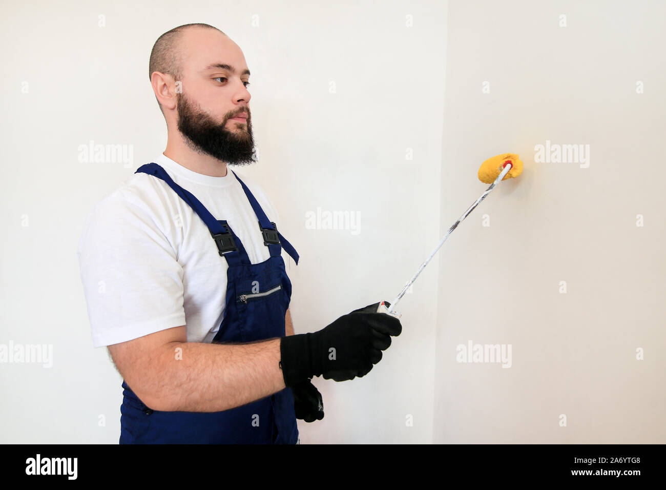 Travailleur de la construction et l'homme à faire terminer la rénovation à l'appartement. À l'aide de rouleau à peindre peintre peinture brosse de mur avec la couleur jaune. Banque D'Images
