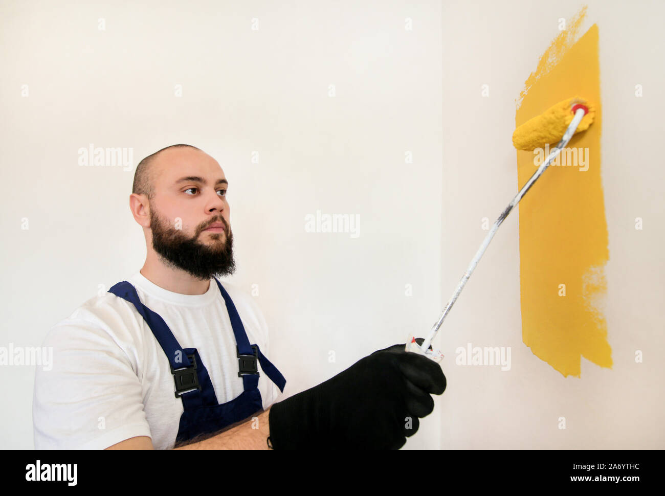 Travailleur de la construction et l'homme à faire terminer la rénovation à l'appartement. À l'aide de rouleau à peindre peintre peinture brosse de mur avec la couleur jaune. Banque D'Images
