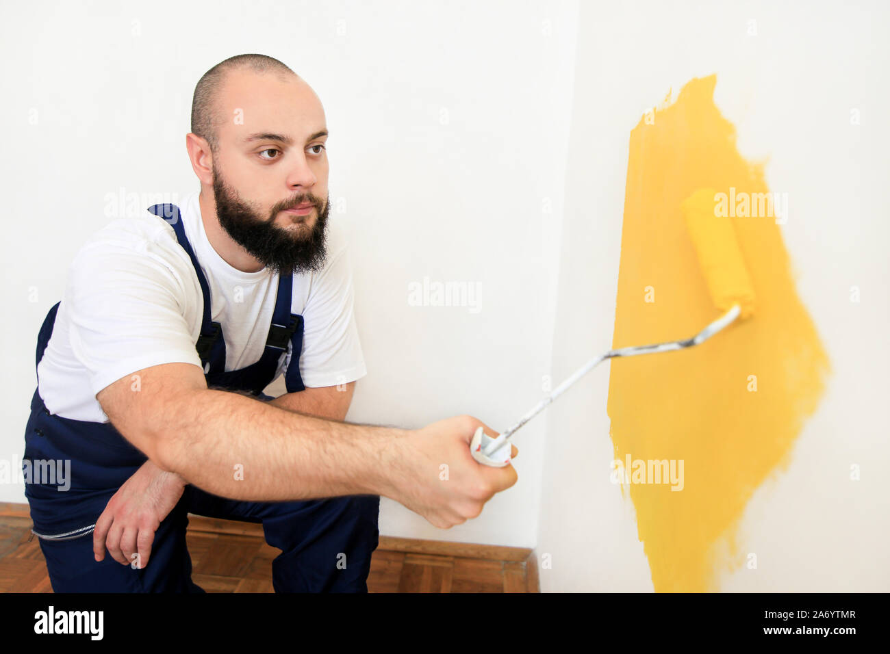 Travailleur de la construction et l'homme à faire terminer la rénovation à l'appartement. À l'aide de rouleau à peindre peintre peinture brosse de mur avec la couleur jaune. Banque D'Images