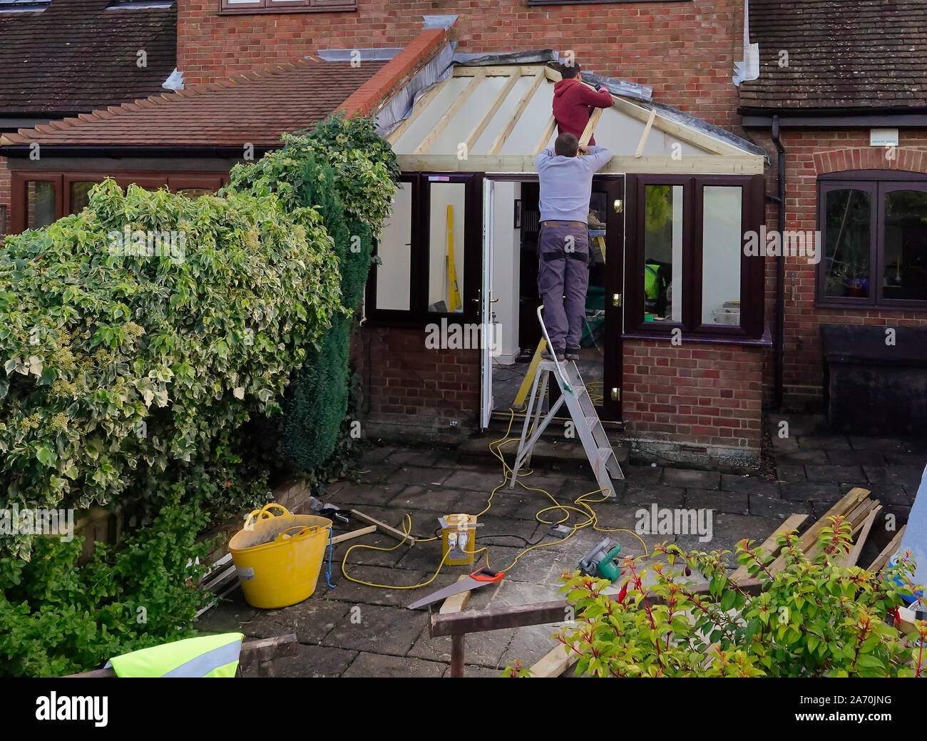 Ouvriers construire un toit sur une véranda extension sur une maison en brique rouge Banque D'Images