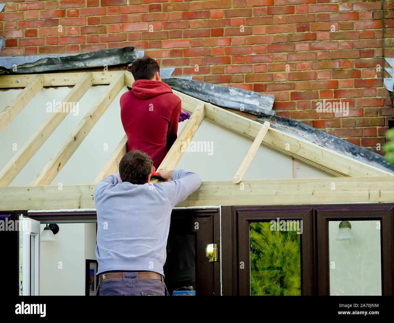 Ouvriers construire un toit sur une véranda extension sur une maison en brique rouge Banque D'Images