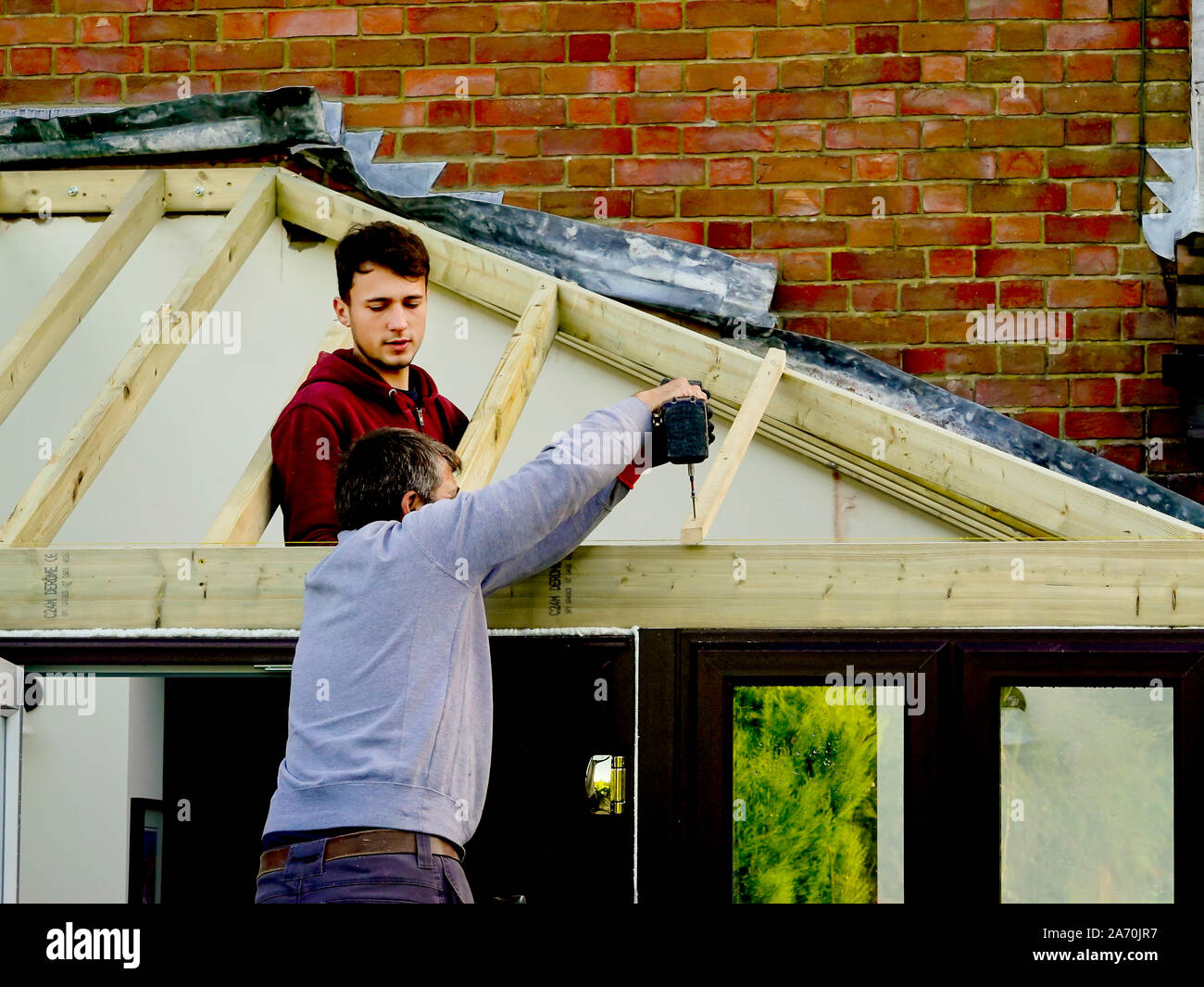 Ouvriers construire un toit sur une véranda extension sur une maison en brique rouge Banque D'Images