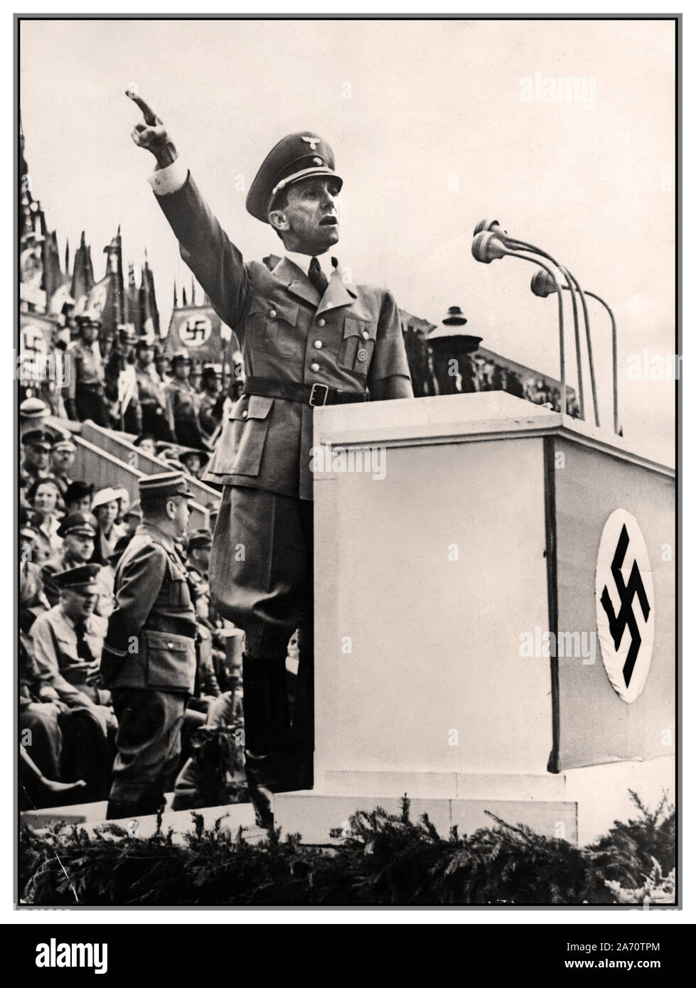 Vintage WW2 1930 image de Dr Joseph Goebbels Ministre de la propagande nazi allemand fait un discours sur un podium avec la croix gammée nazie sur l'Allemagne avant affiche l'emblème Banque D'Images