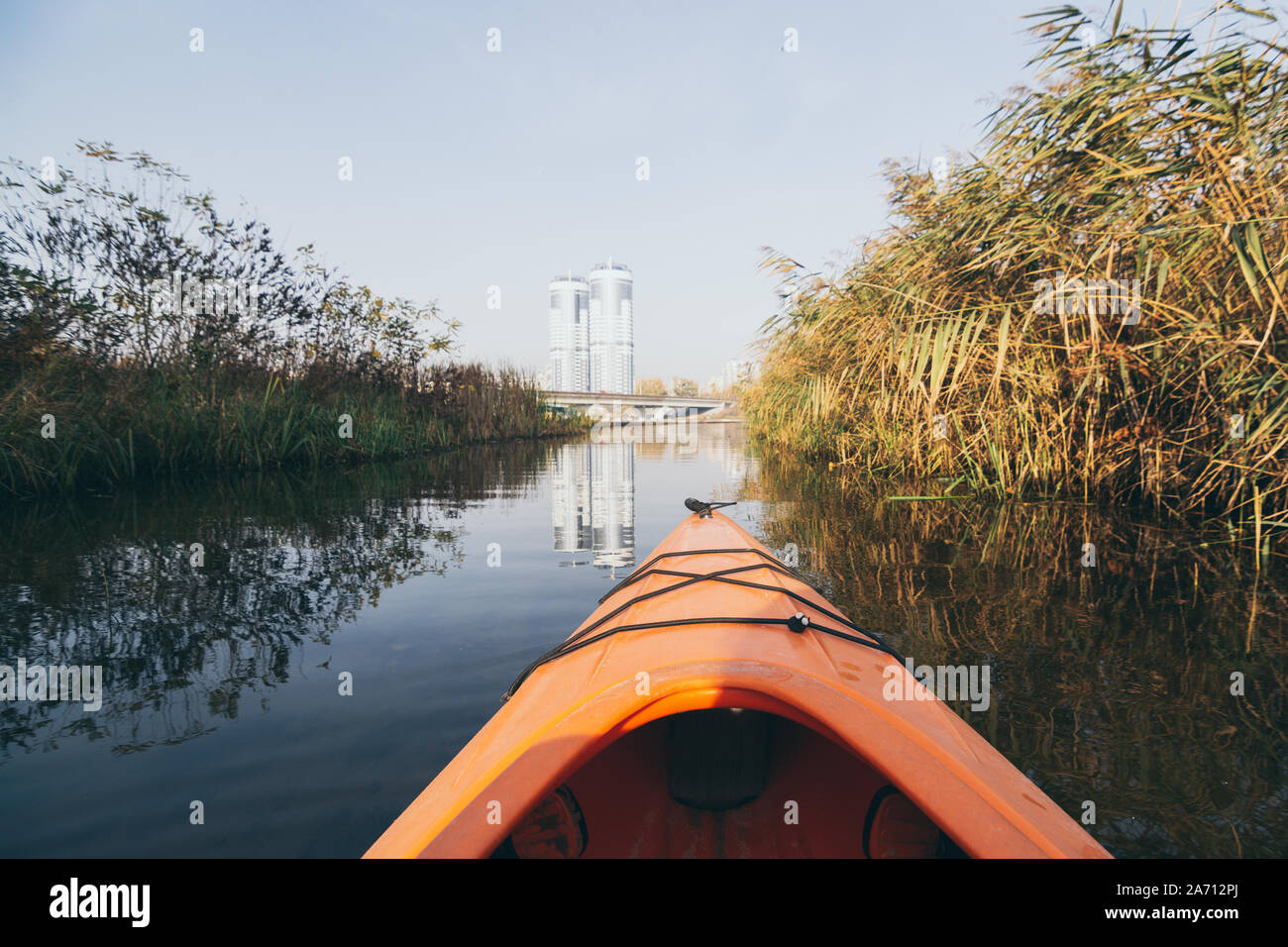 Nez rouge d'Aviron Kayak vers les bâtiments modernes à travers la forêt sur les eaux du Dniepr à Kiev, Ukraine. Banque D'Images