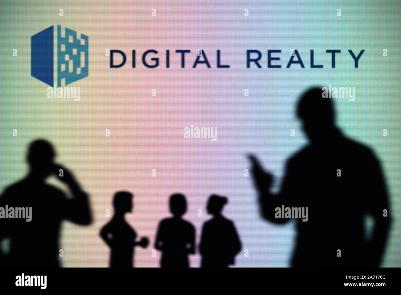 Le logo de Digital Realty est vu sur un écran LED à l'arrière-plan tandis qu'une silhouette personne utilise un smartphone (usage éditorial uniquement) Banque D'Images