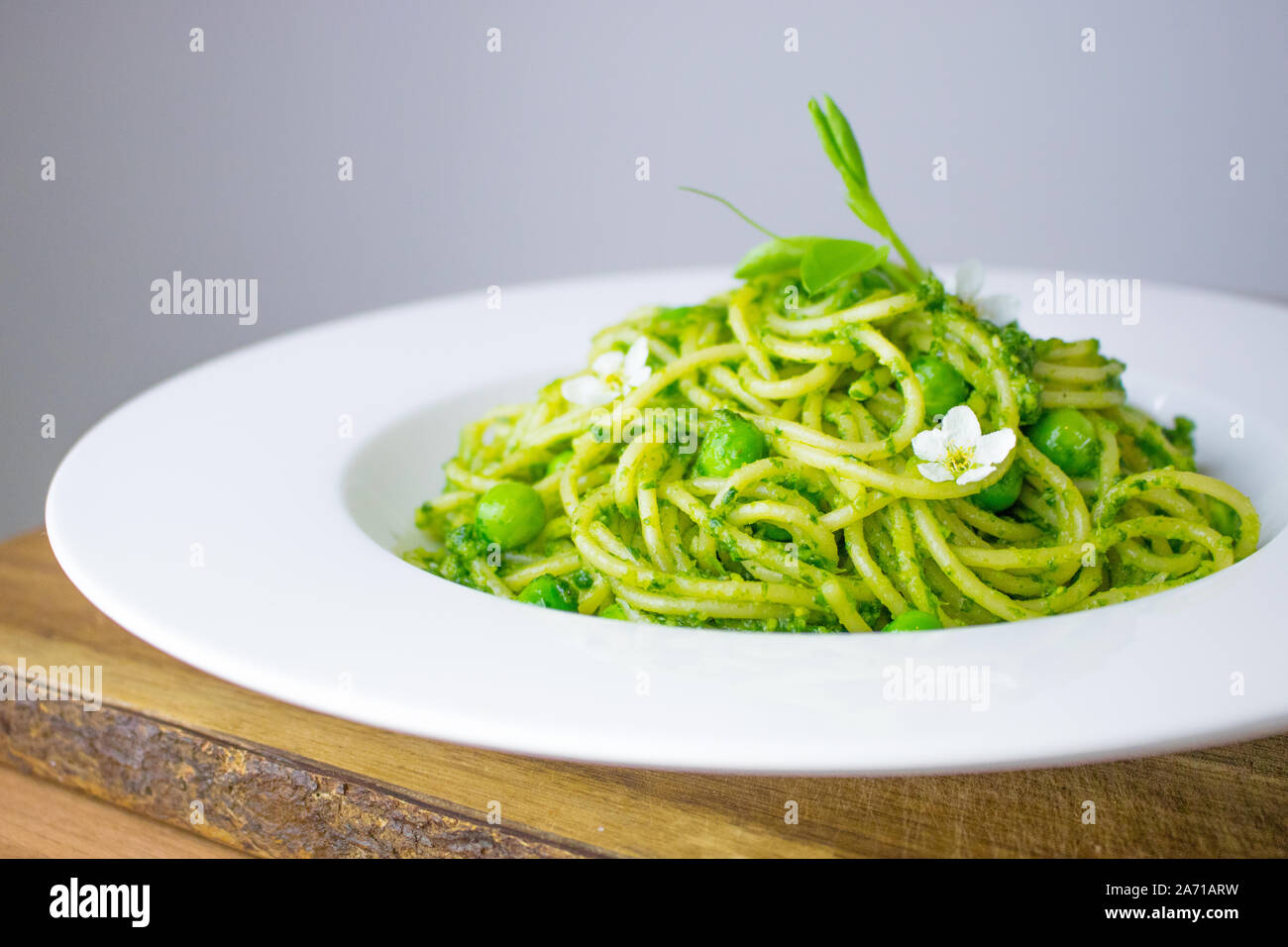 La photographie culinaire de pâtes spaghetti avec rampe vert clair/ pesto à l'ail sauvage, des pois et des petites fleurs blanches pour la garniture. Banque D'Images