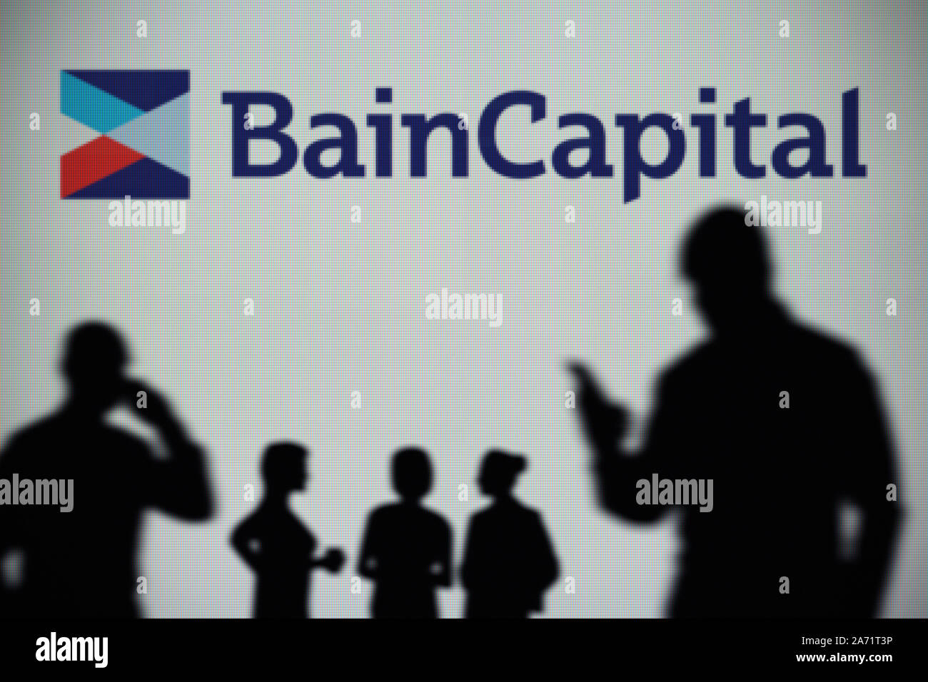 Le Bain Capital logo est visible sur un écran LED à l'arrière-plan tandis qu'une silhouette personne utilise un smartphone (usage éditorial uniquement) Banque D'Images