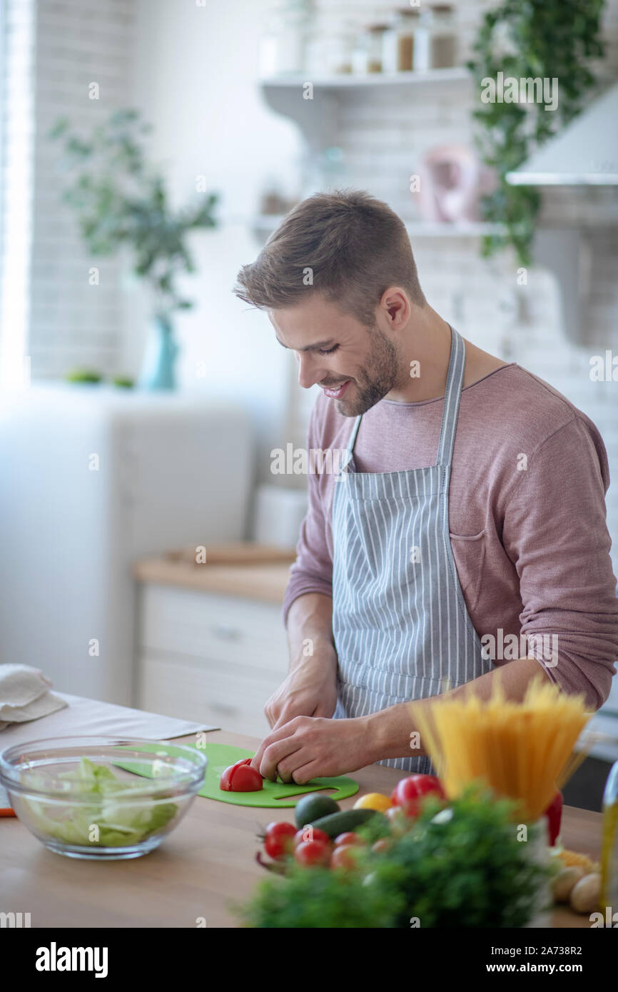 Homme barbu souriant joyeux sentiment salade pendant la cuisson Banque D'Images