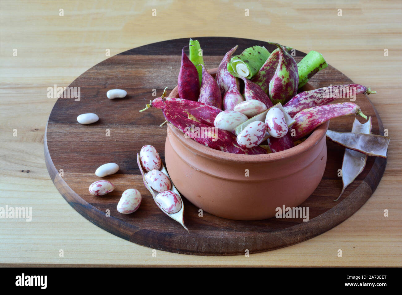 Bio frais, haricots colorés dans une cuvette d'argile, au rond de couleur sombre et planche à découper en noyer Banque D'Images