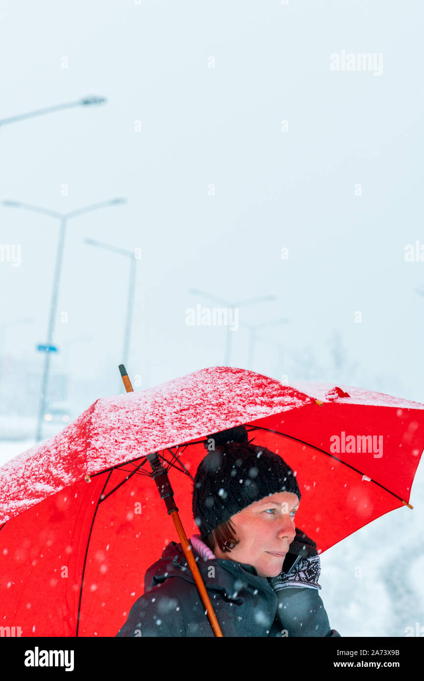 Agréable Woman talking on mobile phone sous parapluie rouge tout en se tenant dans la rue en hiver neige Banque D'Images
