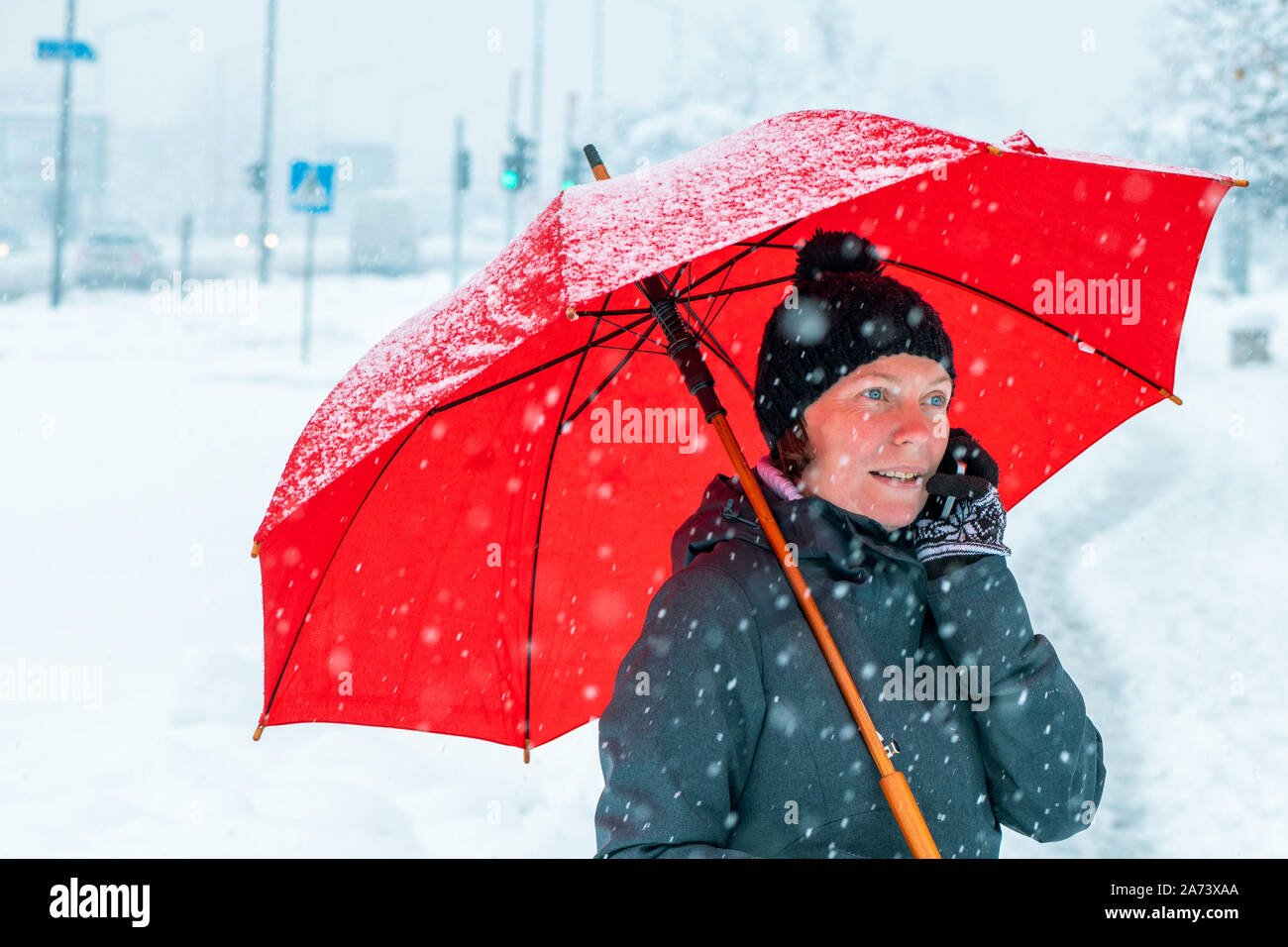 Quartier animé de Woman talking on mobile phone sous parapluie rouge tout en se tenant dans la rue en hiver neige Banque D'Images