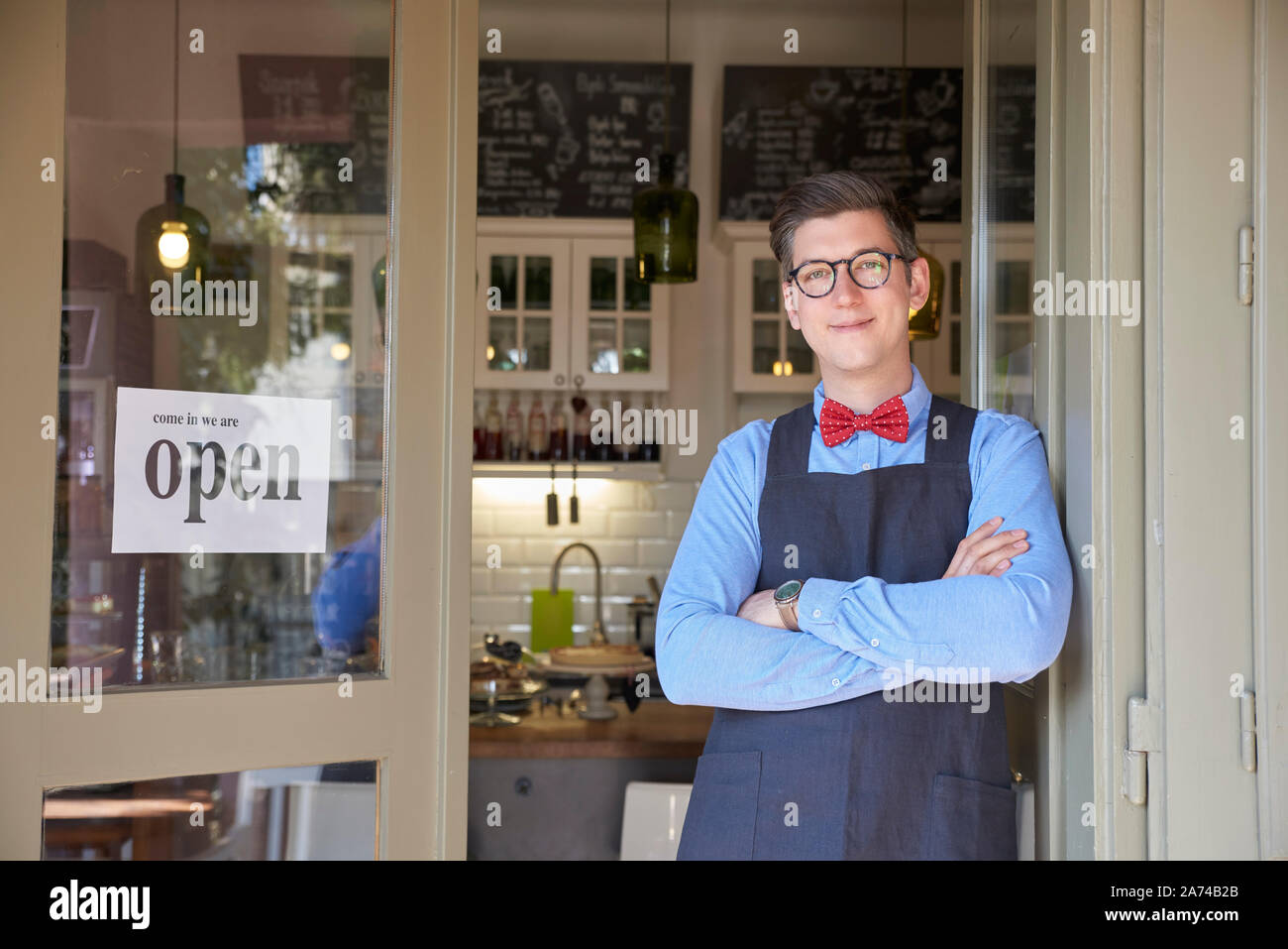 Portrait de propriétaire de petite entreprise jeune homme debout avec les bras croisés dans son café shop entrée. Banque D'Images