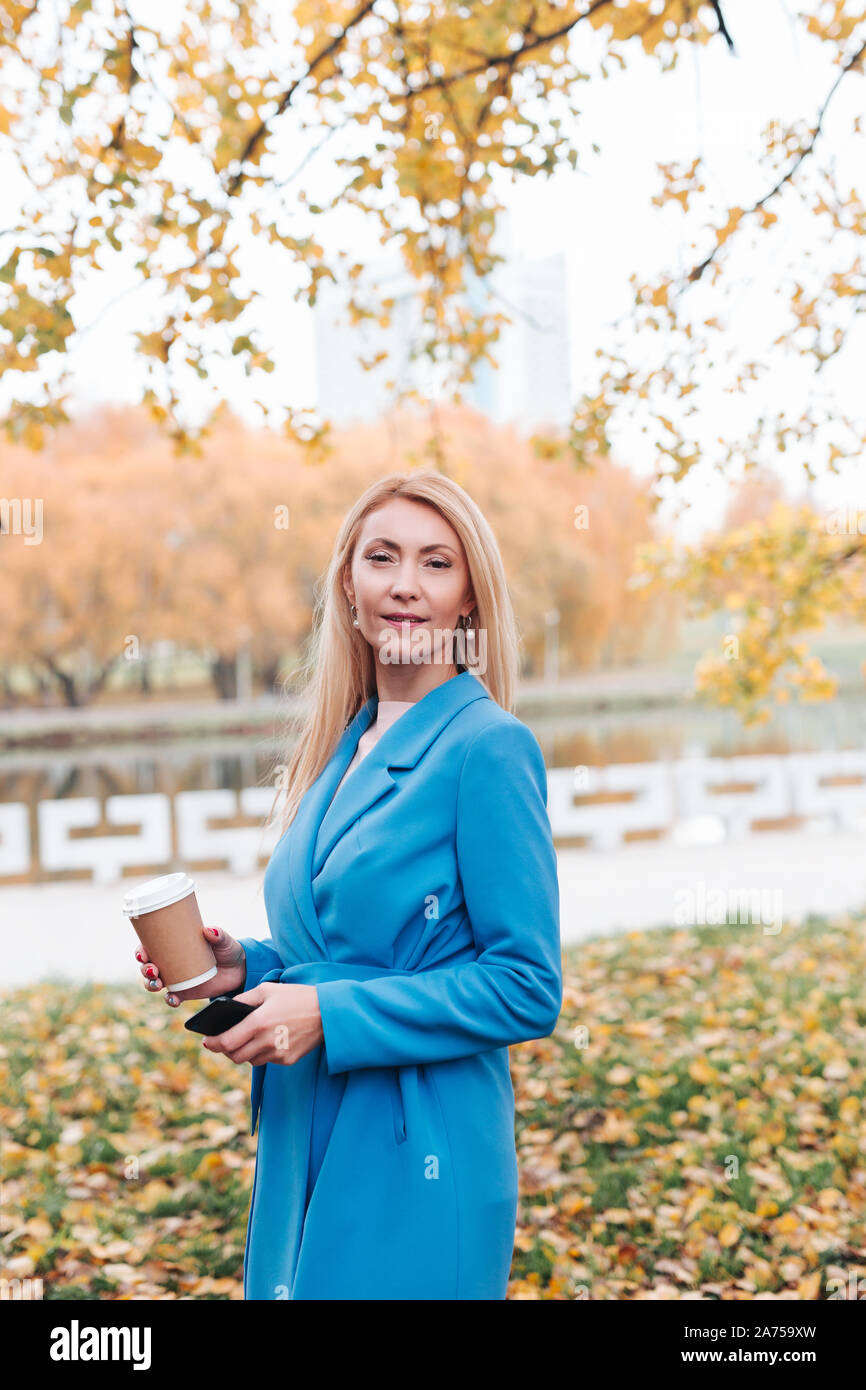 Belle blonde élégante femme debout dans un parc en automne Banque D'Images