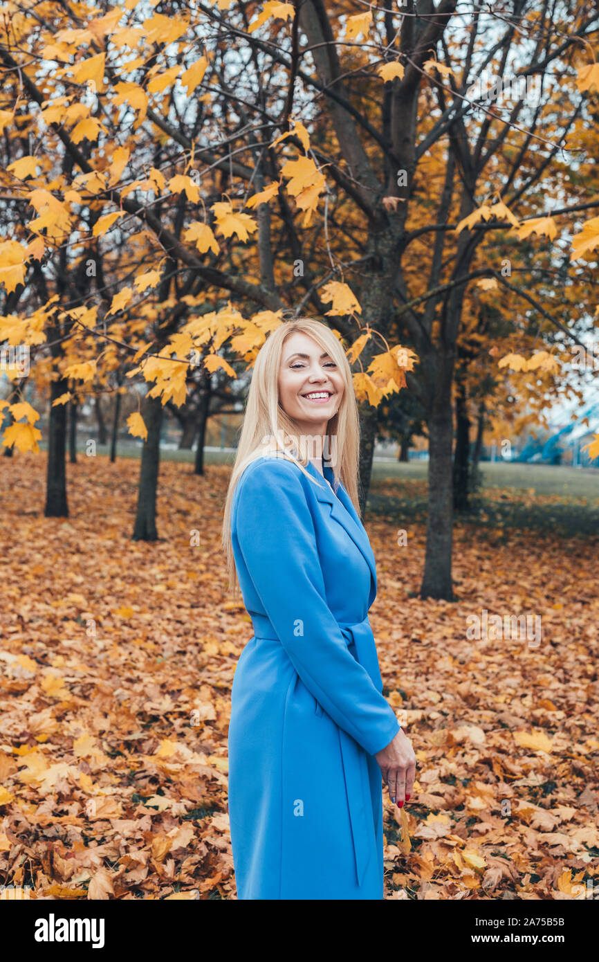 Smiling blonde mature woman looking at camera in autumn park Banque D'Images