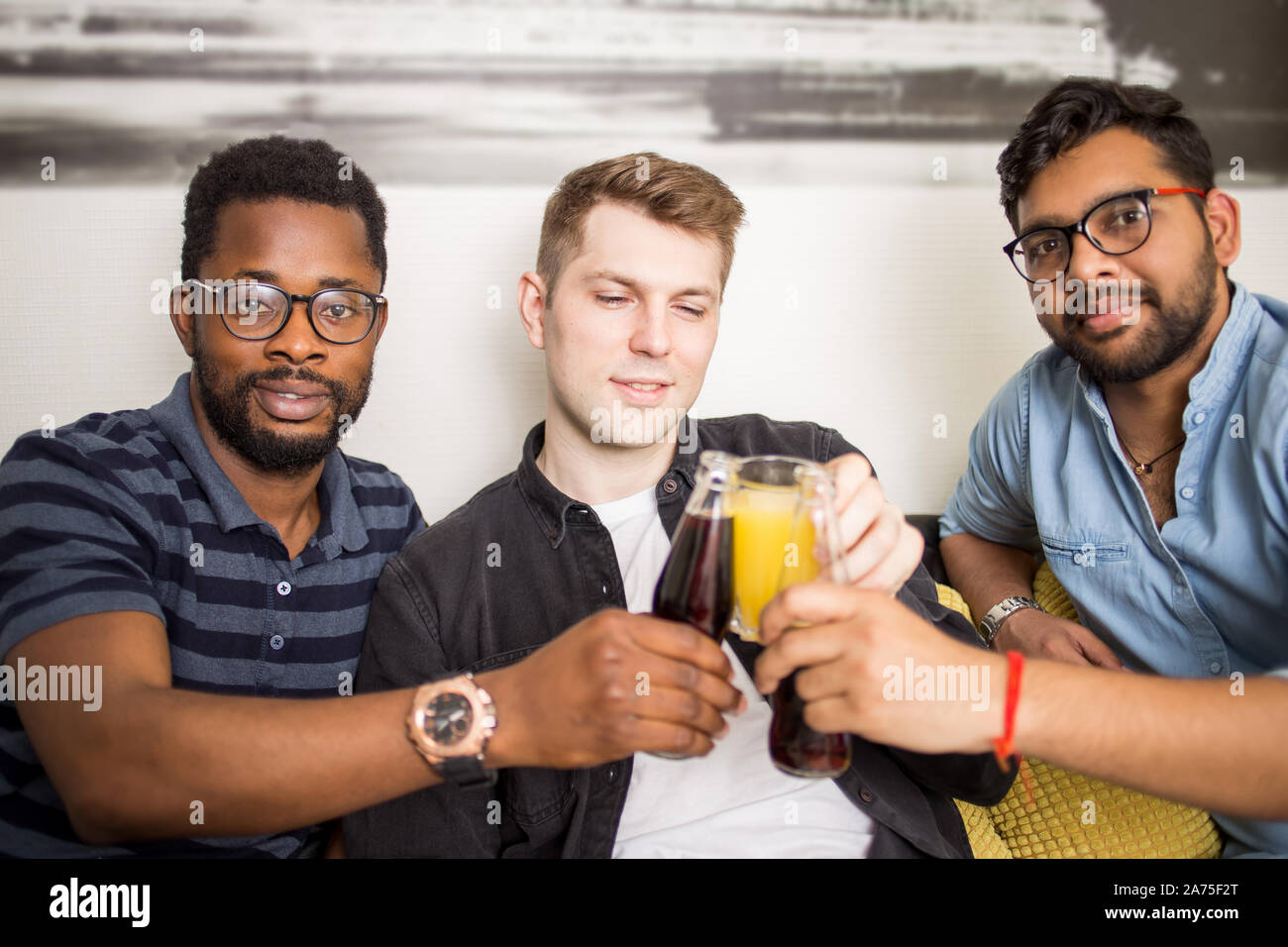 Closeup portrait de trois beaux mâles multi ethnic friends en tenues décontractées tintement des bouteilles de boissons smiling at camera. Les gens, hommes, leis Banque D'Images