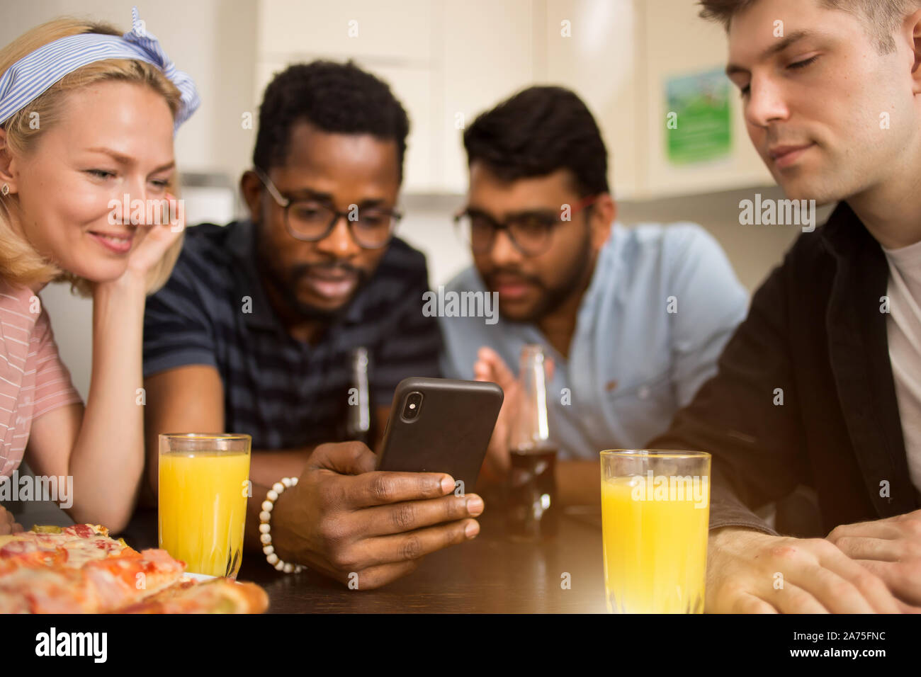 Quatre amis assis à table, de manger des pizzas, boivent des boissons alcoolisées, la lecture de message texte sur smartphone, l'essai de nouvelles application téléphone ensemble. Mult Banque D'Images
