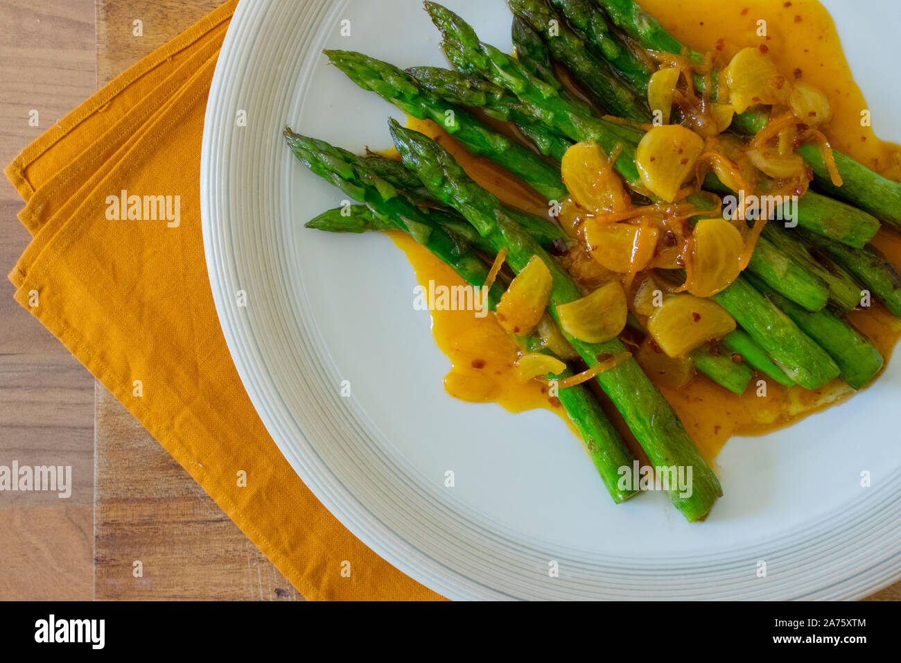 La photographie culinaire d'asperges sautées vert sur une plaque blanche avec orange et sauce à l'ail. Banque D'Images