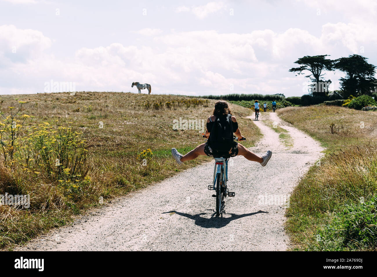 Pretty young woman riding bicycle in a country road avec ses jambes en l'air dans l'île de Batz Banque D'Images