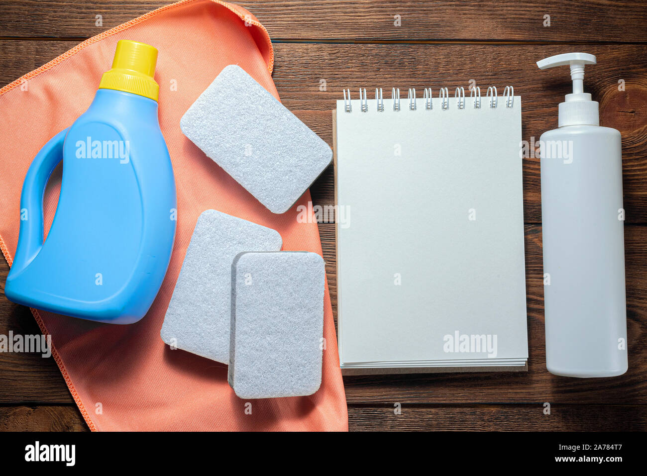 L'offre de lavage, adoucisseur, détergent, linges à vaisselle et le bloc-notes page blanche sur table en bois. Conseils à la personne des maquettes. Banque D'Images