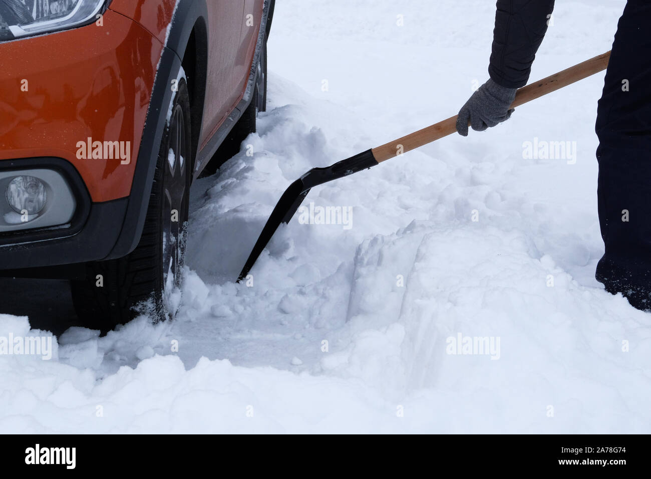 L'hiver, la neige, véhicule. Le brossage et l'homme à côté de pelleter la neige voiture orange en hiver après des chutes de neige. Pelle à main. Banque D'Images