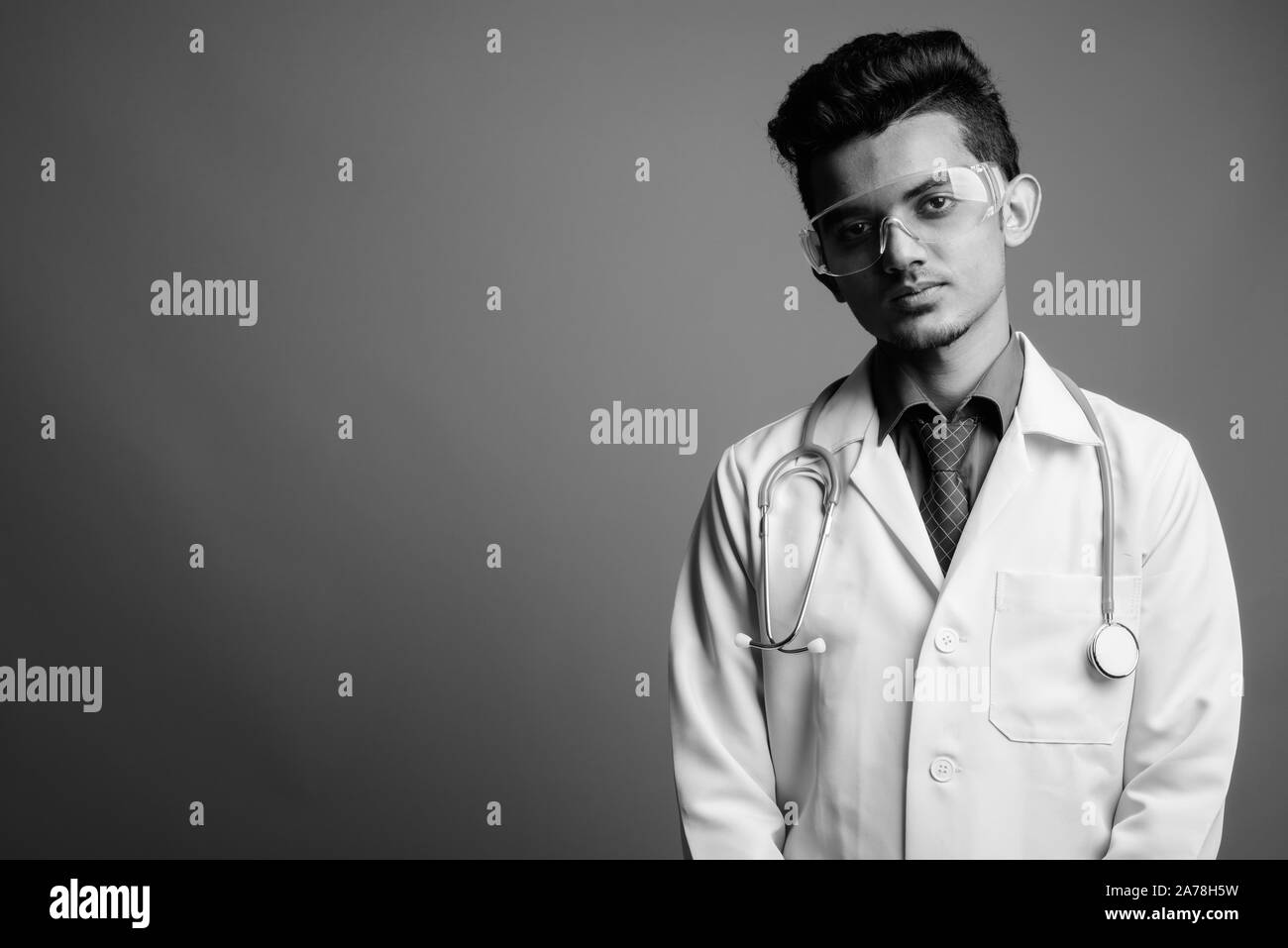 Jeune Indien médecin homme portant des lunettes de protection contre l'arrière-plan gris Banque D'Images