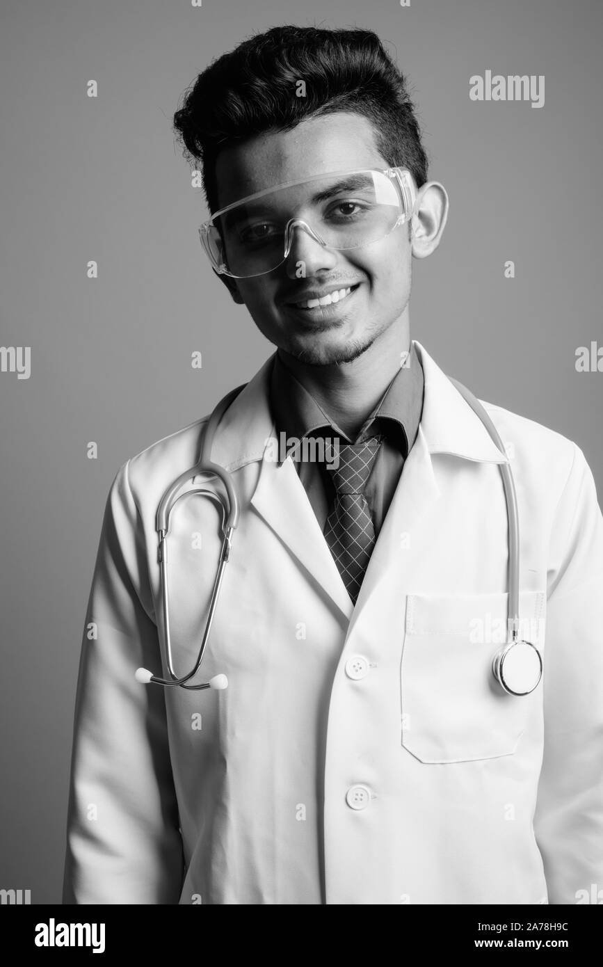 Jeune Indien médecin homme portant des lunettes de protection contre l'arrière-plan gris Banque D'Images