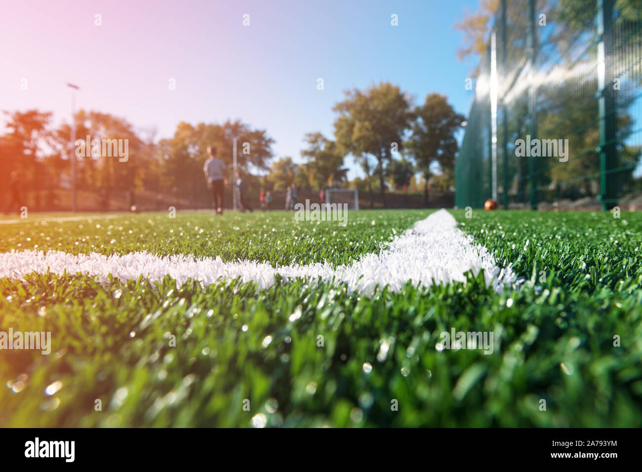 Terrain de football sur une journée ensoleillée avec gradient. Les enfants jouent au soccer. Point bas, avec effet bokeh. Nouveau gazon artificiel avec un marquage blanc ligne. Banque D'Images