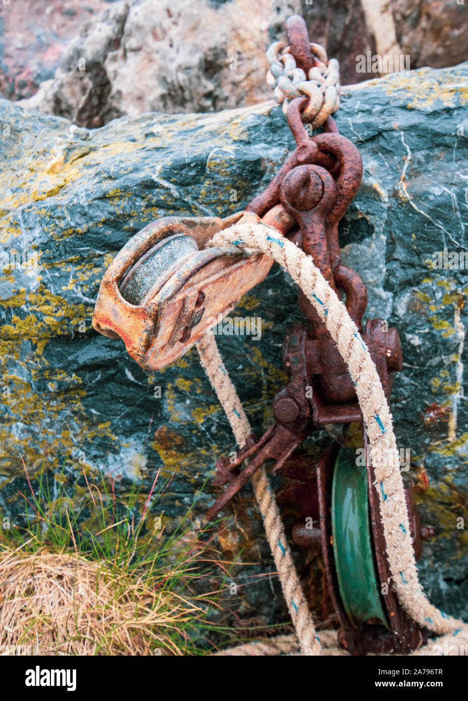 Chaîne rouillée sur green rock avec poulie et corde blanche. Banque D'Images