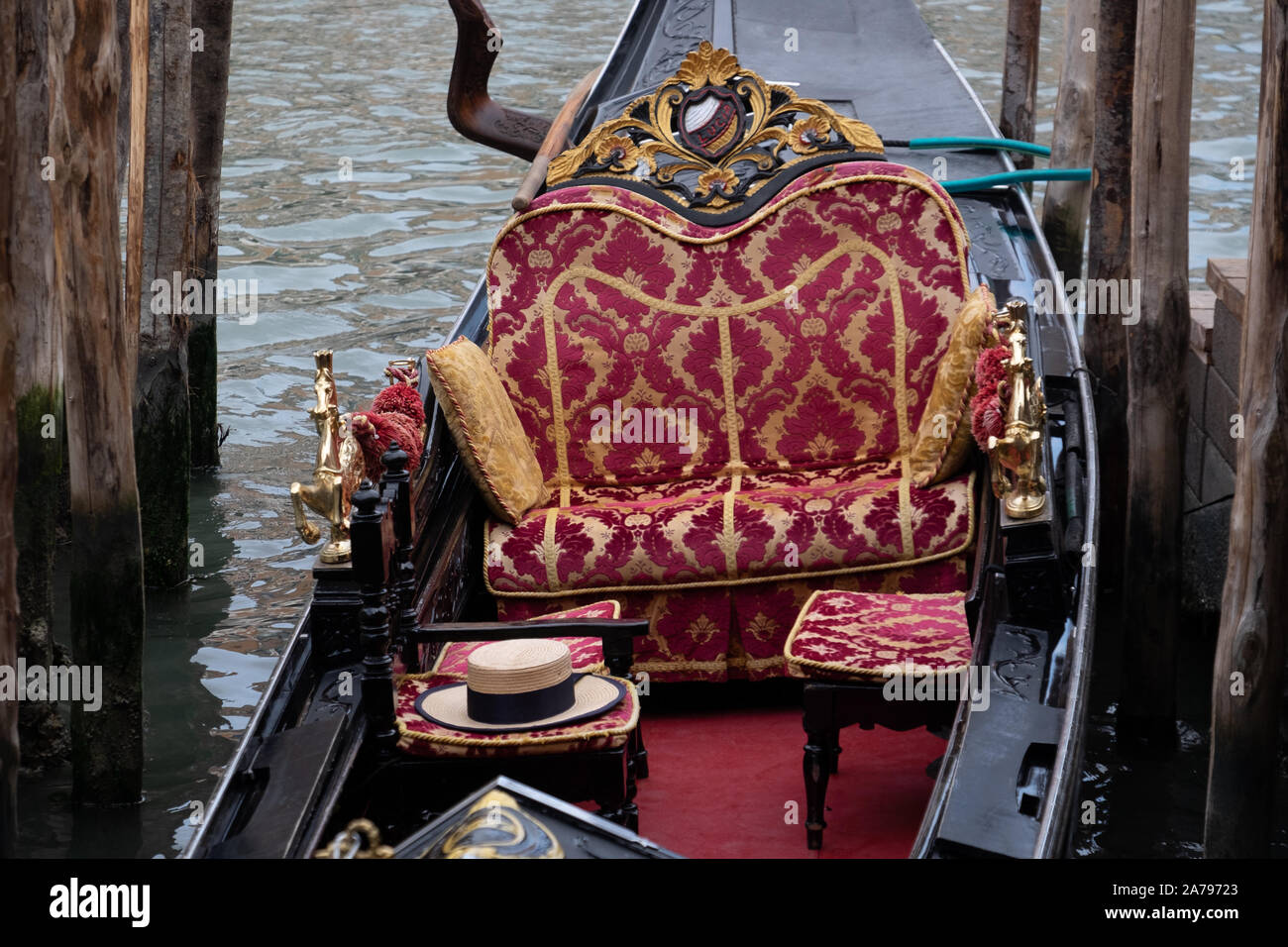 De magnifiques sièges moelleux dans les rouges et ors détails de l'intérieur d'une gondole traditionnelle avec canotier de paille sur un côté. Banque D'Images