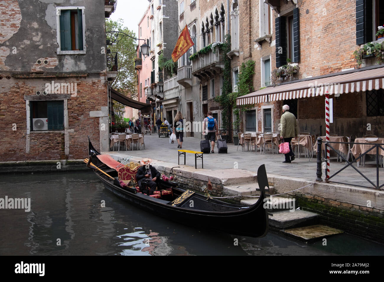 Gondole et gondolier amarré à côté d'étapes sur canal interne et de Venise, la lecture de son téléphone portable, en attente de son prochain billet, ignorés par les passants. Banque D'Images