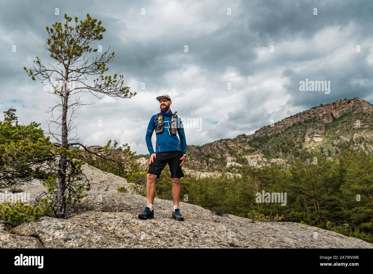 Coureur masculin debout sur un rocher dans les montagnes. Exécute l'athlète dans les montagnes au milieu des rochers. L'homme en maillot bleu et short noir à l'extérieur formation Banque D'Images