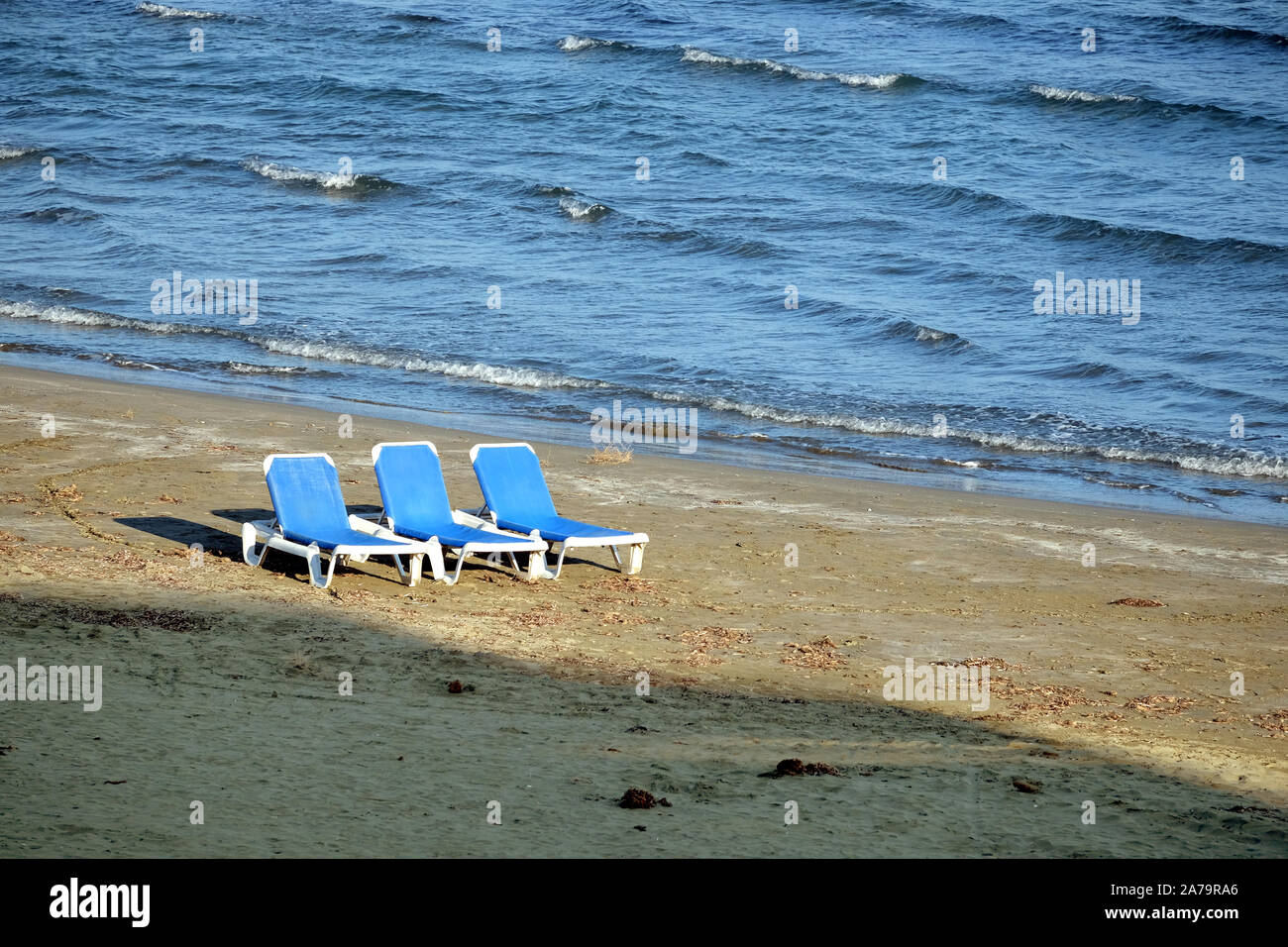 Basse saison. Plage de sable vide avec trois chaises longues en plastique blanc sur le sable près de l'avant-garde seacoast mer avec de petites vagues sur la journée ensoleillée Banque D'Images