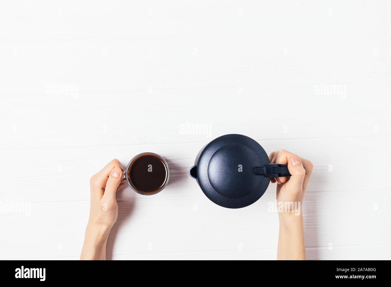 Geyser cafetière et tasse d'expresso fraîchement préparé dans les mains sur la table en bois blanc, avec copie espace, vue du dessus Banque D'Images