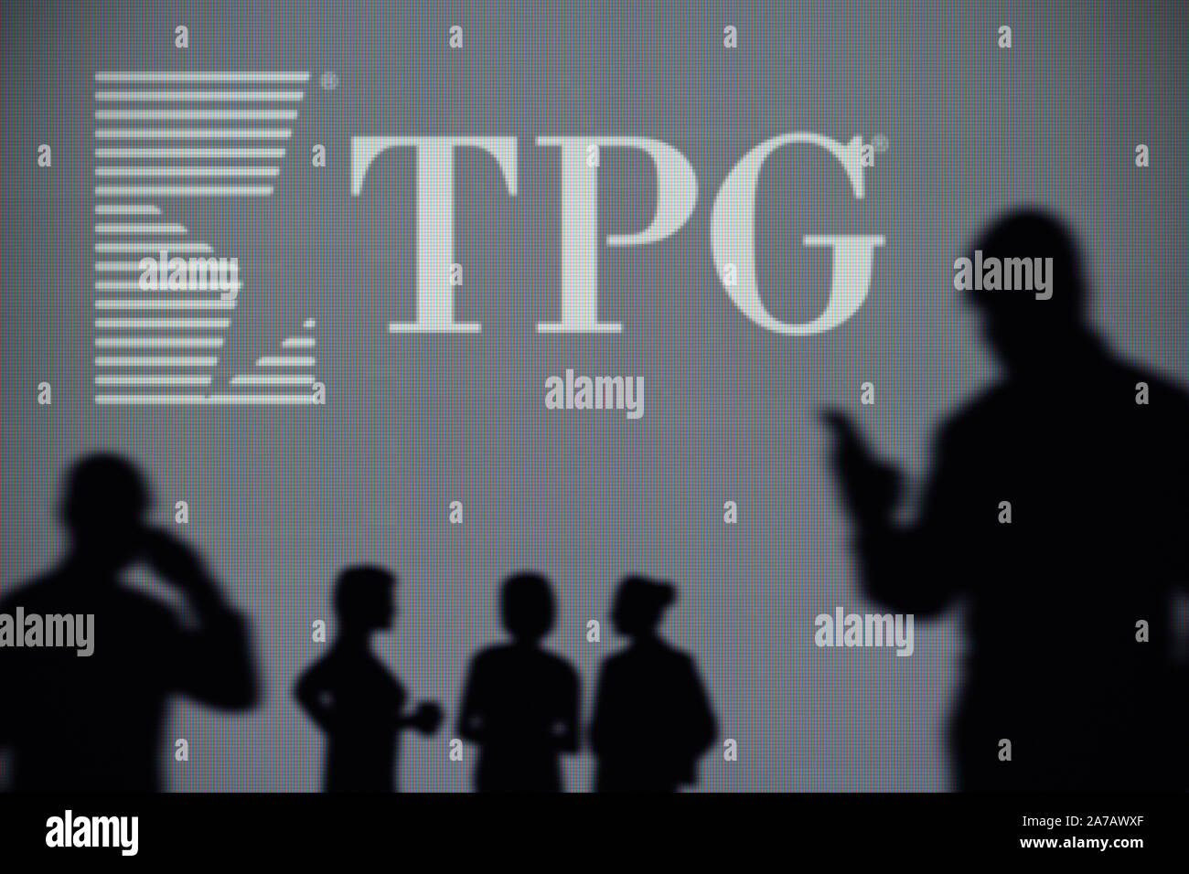 Le TPG Capital logo est visible sur un écran LED à l'arrière-plan tandis qu'une silhouette personne utilise un smartphone (usage éditorial uniquement) Banque D'Images