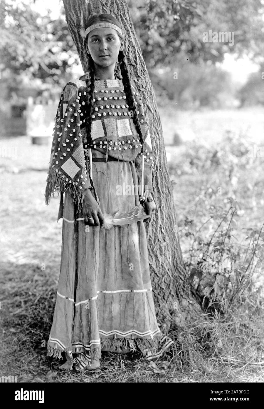 Portrait, pleine longueur, debout par arbre, bandeau de perles de perles, robe de daim Banque D'Images