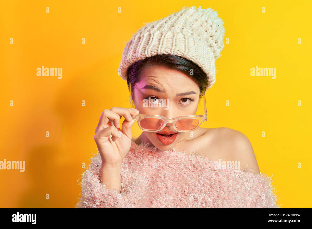 Fille asiatique émotionnel avec le maquillage coloré posant sur fond jaune avec des lunettes. Une photo de femme dans le quartier branché d'étonnement manteau de fourrure. Banque D'Images