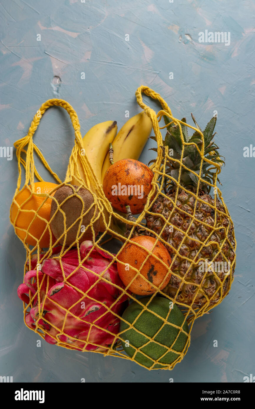 Concept zéro déchet, sacs en textile mesh avec fruits frais tropicaux : mangue, ananas, dragon, kiwi, banane, fruits de la passion sur fond bleu clair Banque D'Images
