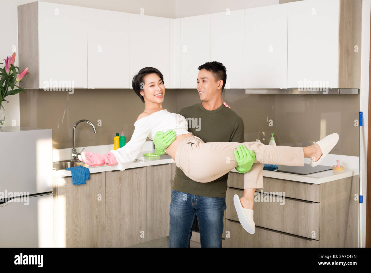 Jeune mari embrassant sa femme pendant le nettoyage de la cuisine. Banque D'Images