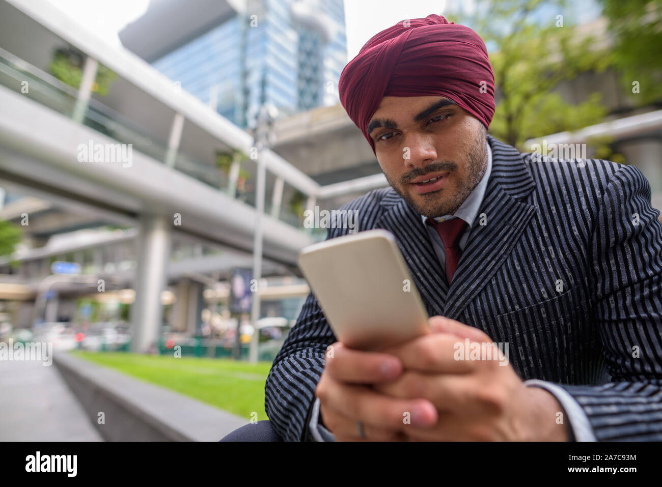 Homme d'affaires indien assis à l'extérieur en ville lors de l'utilisation de téléphone mobile Banque D'Images