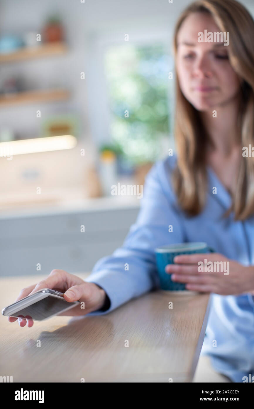 Femme inquiète de l'utilisation excessive des médias sociaux portant sur téléphone mobile sur la table Banque D'Images