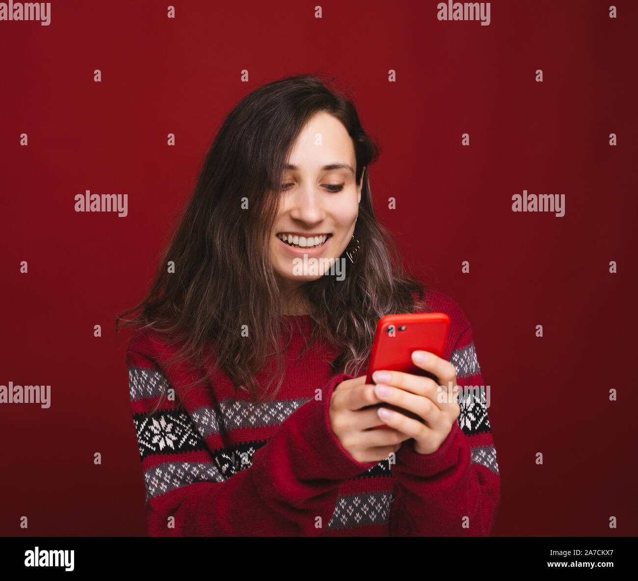 Cheerful yougn pull femme en rouge en utilisant son smartphone sur fond rouge Banque D'Images