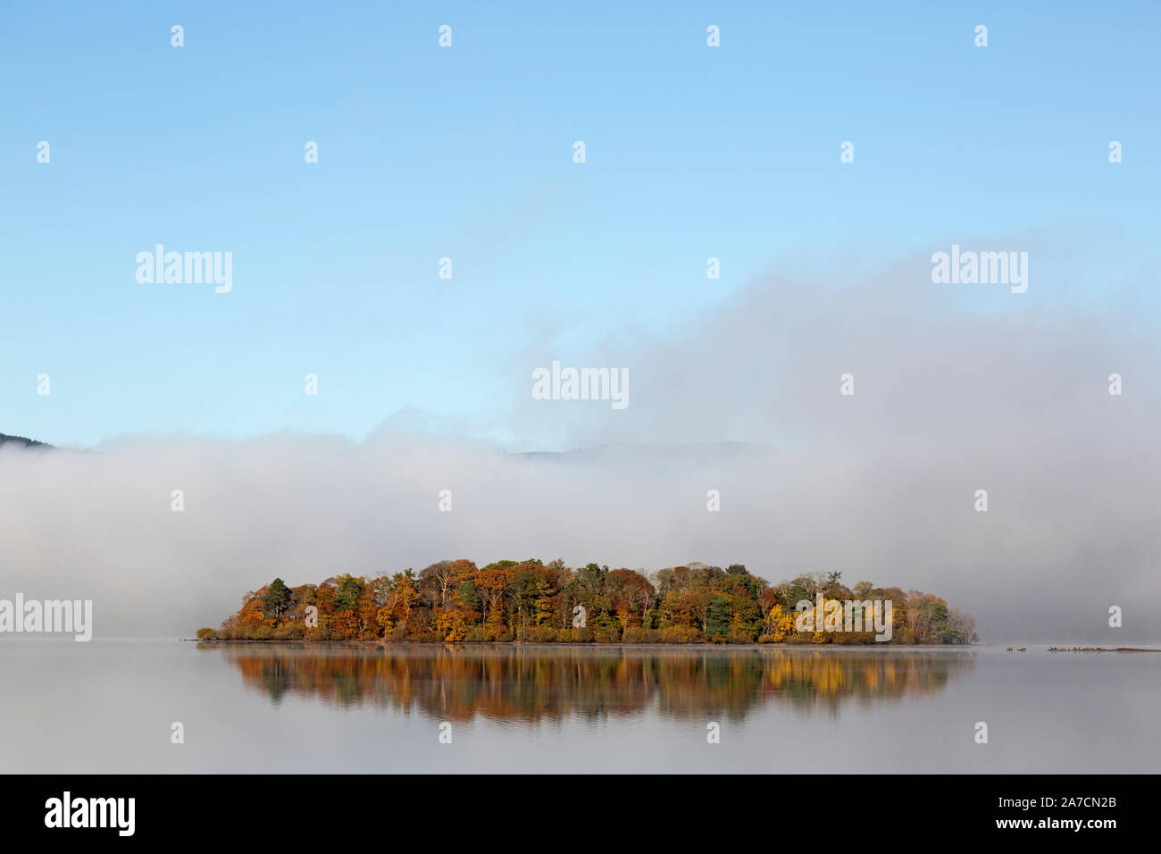 Derwent Water dans le Parc National du Lake District, Angleterre, brume matinale enveloppant une petite île, avec des arbres en couleurs de l'automne. Banque D'Images