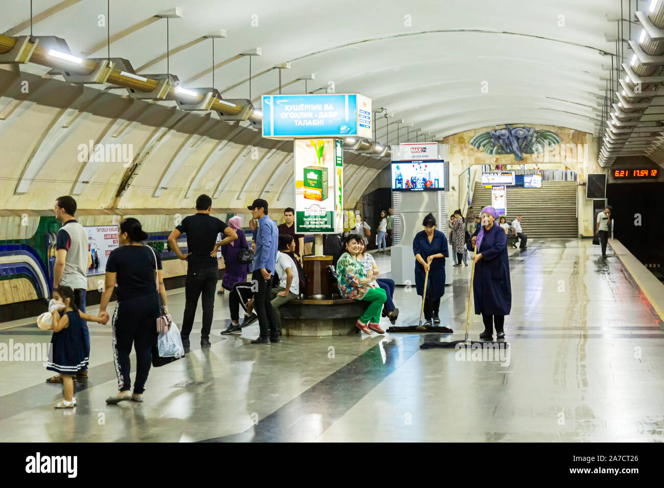 Deux femmes cleaners sweep la plate-forme à Tachkent comme un métro Chorus nombre de passagers assis ou debout autour d'attente pour un train d'arriver Banque D'Images